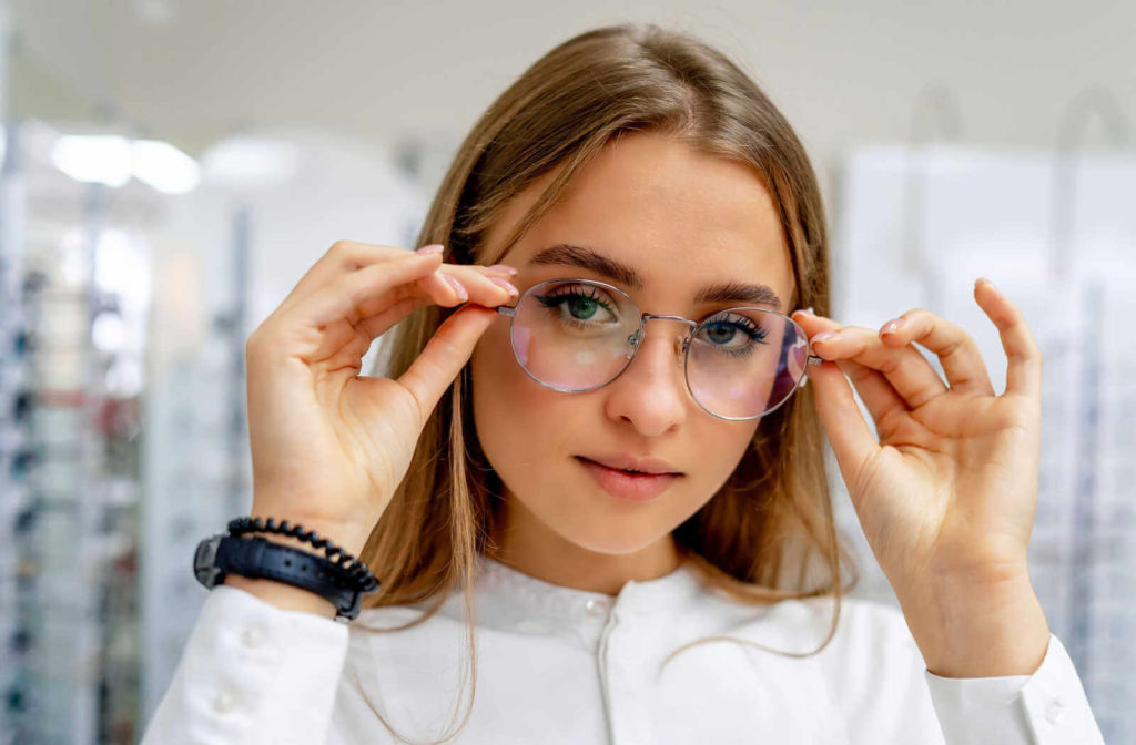 A teenager in a white, long-sleeved shirt in an optical shop trying on a pair of eyeglasses.