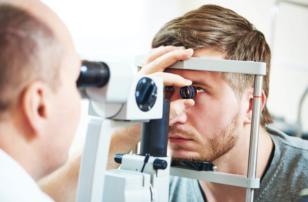 "An optometrist performing an eye examination on a man using a specialized medical device while holding a lens up to the man's eye."