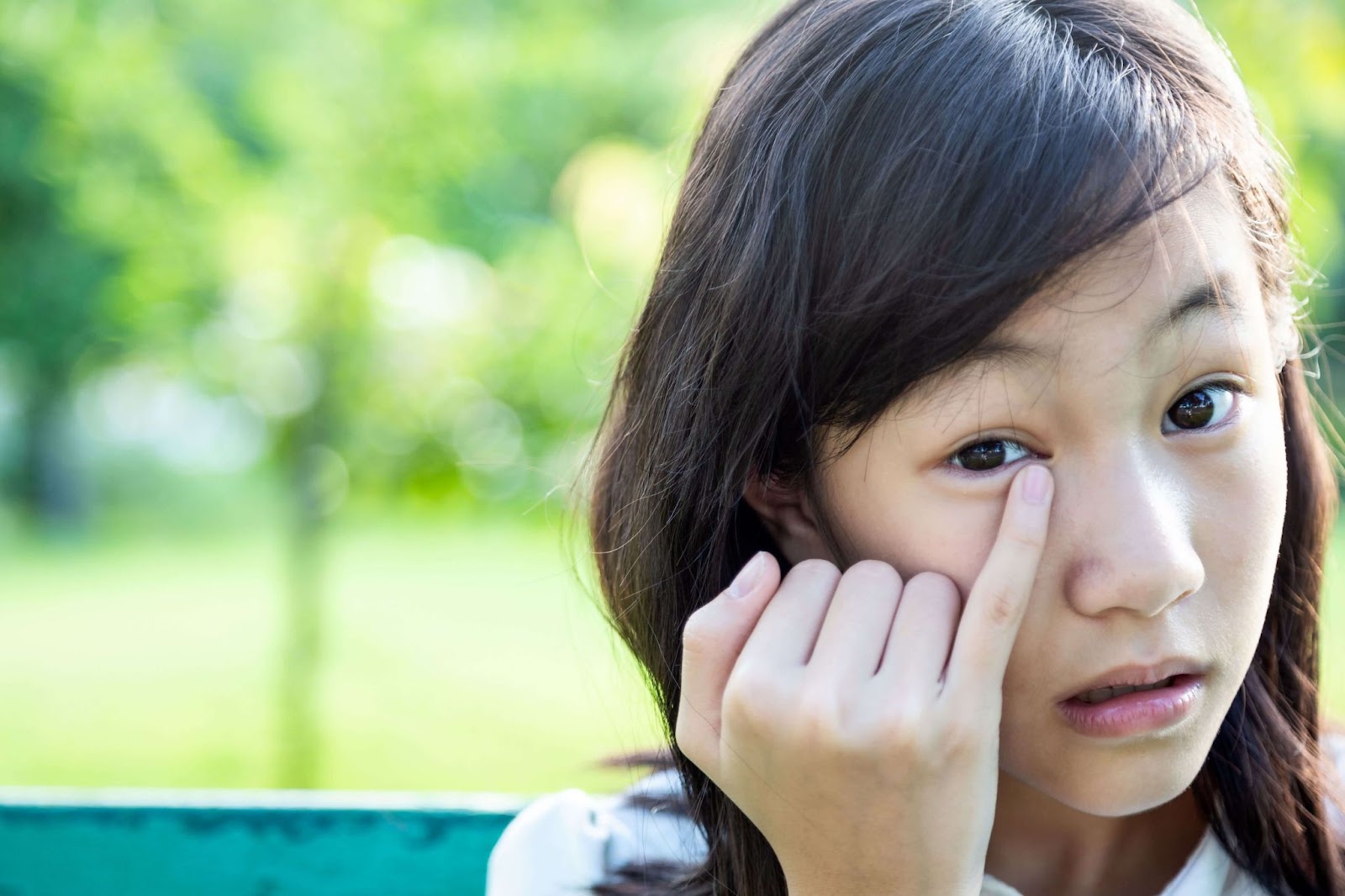 Close-up of a young girl outside rubbing her right eye with her right pinky finger